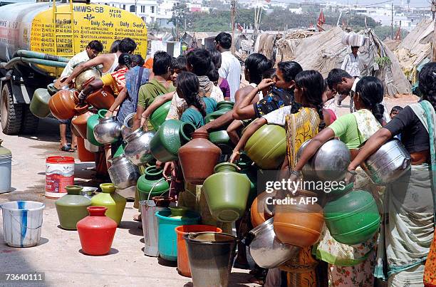 Indian people stand in a line as they wait to fill containers with drinking water supplied by a mobile water vehicle in a slum area in the Saidabad...