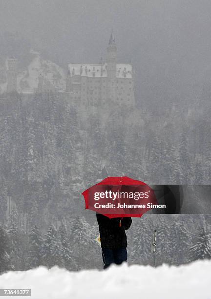 Man with a red umbrella walks in snow with the "fairy tale" Neuschwanstein Castle in the background on March 20, 2007 near Fussen , Germany....