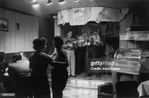 American blugrass musicians Earl Taylor and the Stoney Mountain Boys play instruments and sing as they perform on a small stage as a few people dance...