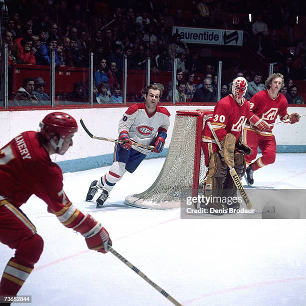 Goaltender Dan Bouchard of the Atlanta Flames and Guy Lafleur of the Montreal Canadiens look on as Randy Manery plays the puck.