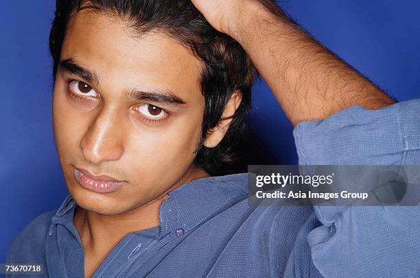 man in blue shirt against blue background, hand on head - pensive indian man stock pictures, royalty-free photos & images