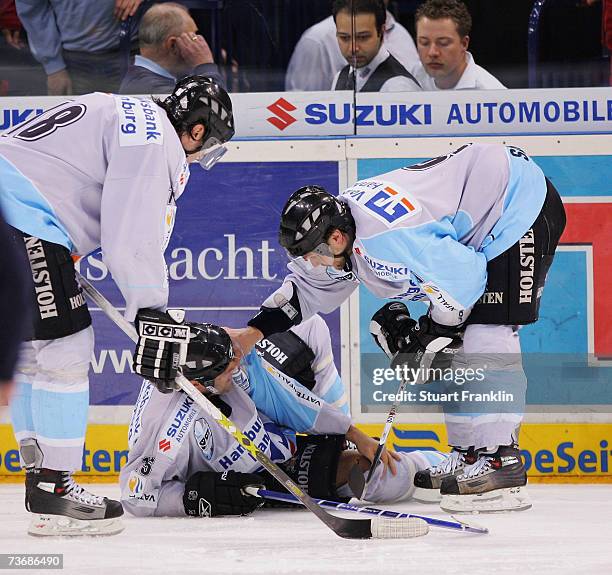 Francois Fortier of Hamburg lies injured as he gets support from Vitalij Aab and Heiko Smazal during the DEL Play Off quarter final match between...