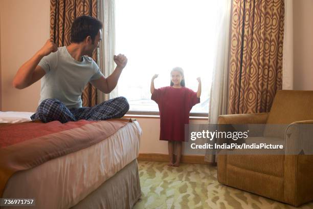 father watching daughter try on his t-shirt in bedroom showing strength - passt nicht stock-fotos und bilder