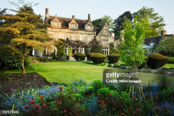 exterior view of a 17th century country house from a garden with flower beds, shrubs and trees. - stately home stock pictures, royalty-free photos & images