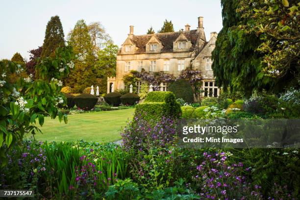 exterior view of a 17th century country house from a garden with flower beds, shrubs and trees. - luxuriant stock-fotos und bilder