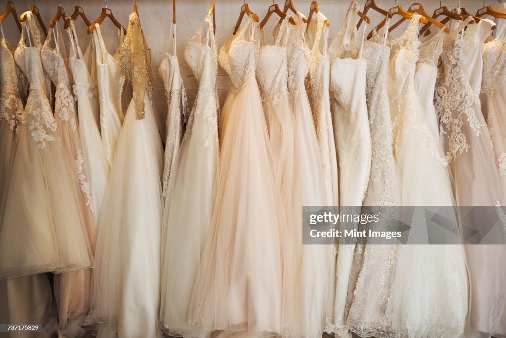 Rows of wedding dresses on display in a specialist wedding dress shop. A variety of colour tones and styles, fashionable lace and boned bodices.