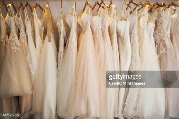 rows of wedding dresses on display in a specialist wedding dress shop. a variety of colour tones and styles, fashionable lace and boned bodices.  - brudklänning bildbanksfoton och bilder