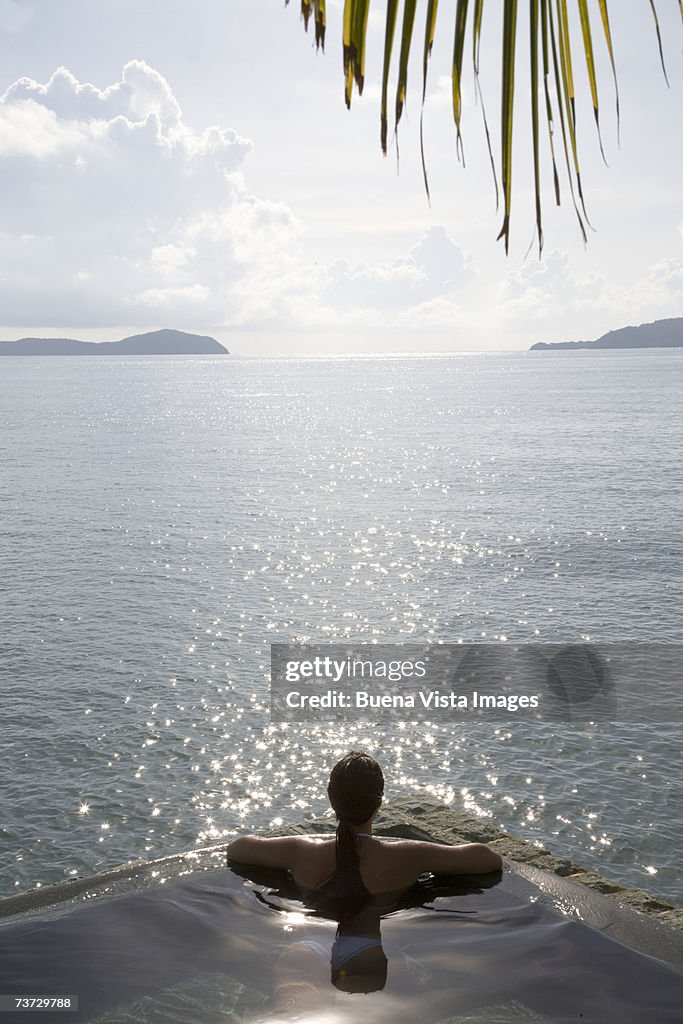 Young woman sitting in infinity pool, rear view