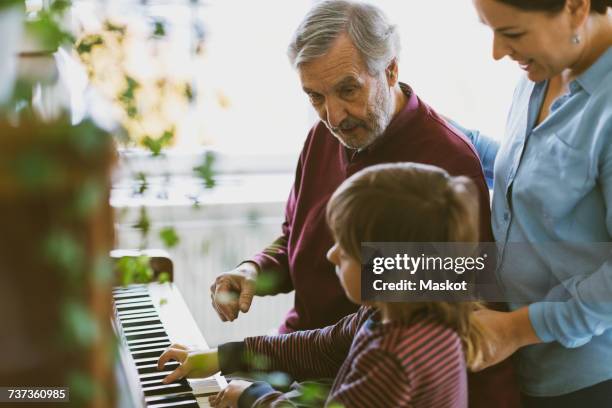 mother and great grandfather looking at boy playing piano in house - learning generation parent child ストックフォトと画像