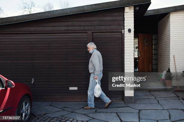 side view of senior man carrying bag while walking by wall - viudo fotografías e imágenes de stock