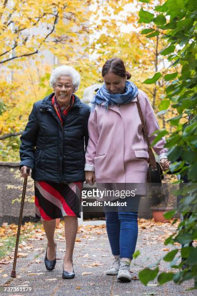 full length of senior woman walking with daughter in park - grandma cane stock pictures, royalty-free photos & images