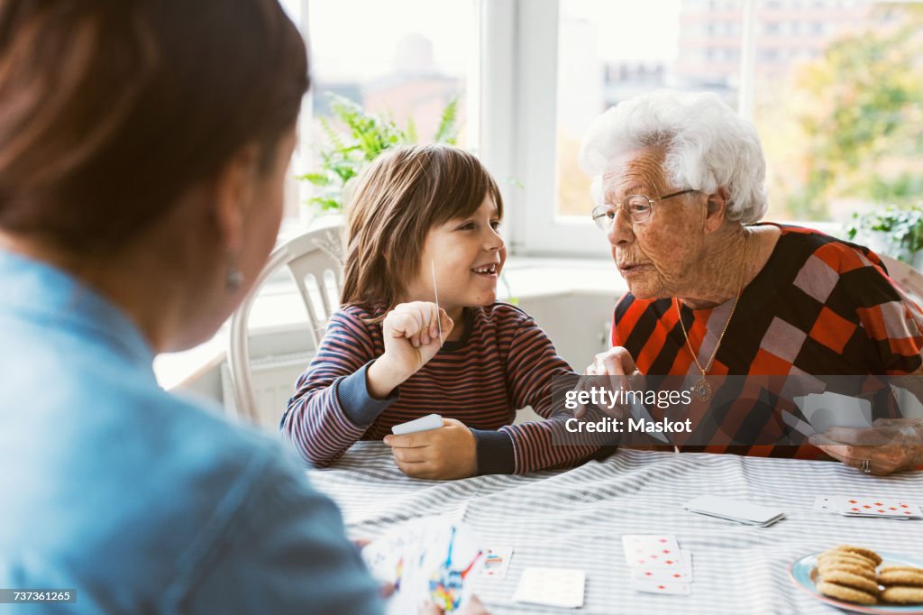 Happy boy showing playing card with great grandmother at home