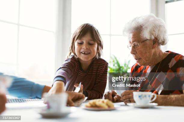 happy boy playing cards with great grandmother and mother at table - visita stock pictures, royalty-free photos & images