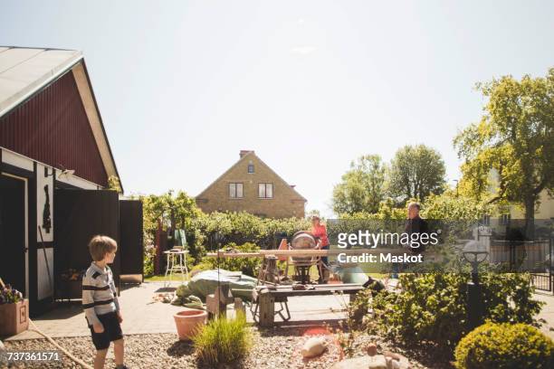 boy looking at grandparents doing carpentry in yard against clear sky - the house film 2017 stock-fotos und bilder