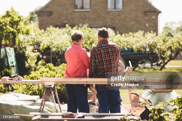 rear view of senior couple standing by wooden plank against house at yard - renovering bildbanksfoton och bilder