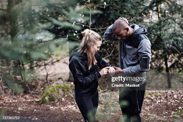 male and female athletes checking smart watch in forest - sport armbinde stock-fotos und bilder