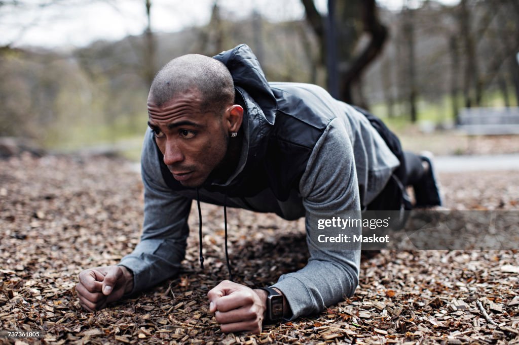 Determined male athlete performing plank position in forest