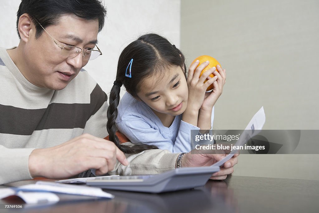 Father explaining a document to daughter holding orange.