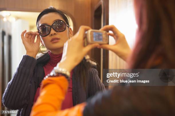 young woman playfully poses as another takes her photo during shopping trip - looking through sunglasses stock pictures, royalty-free photos & images