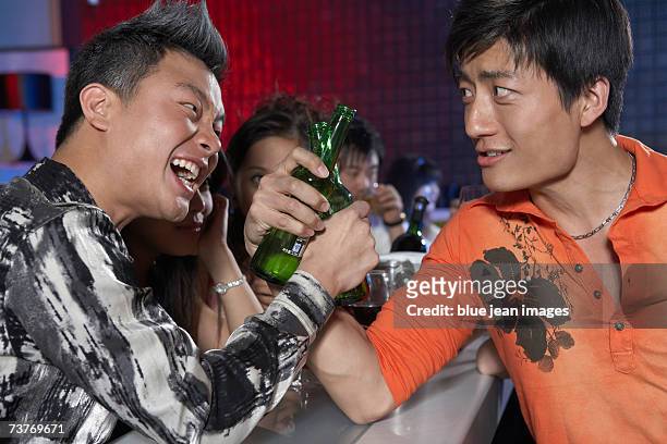 two young men raise bottles in a toast during an evening at the nightclub - beer bottle mouth stock-fotos und bilder