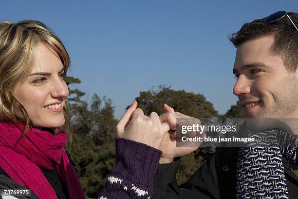 young couple playfully lock fingers together on a bright, sunny day - pinky promise stock pictures, royalty-free photos & images