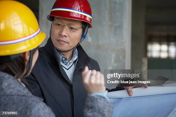 middle age man showing blueprints to woman, front view of man, close up. - beton person close stock-fotos und bilder