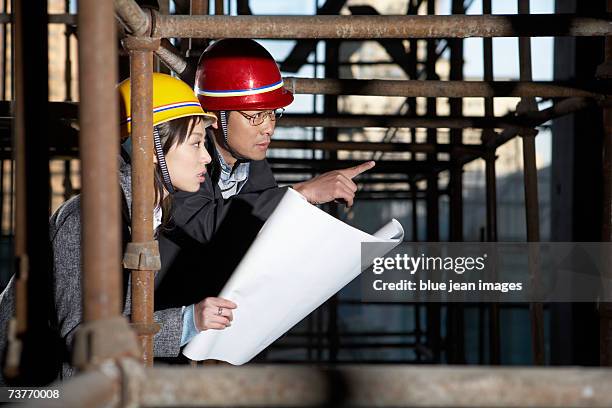 middle age man showing blueprints to young woman, inside scaffolding, man pointing, side profile, close up. - beton person close stock-fotos und bilder