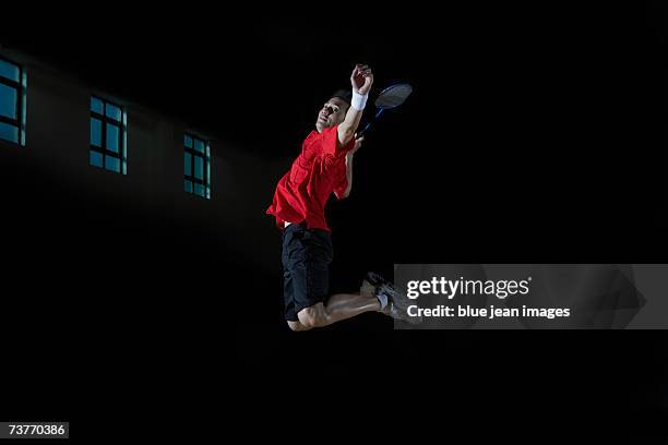 young man leaps high in the air and prepares to smash a shuttlecock during a game of badminton. - badminton smash stock pictures, royalty-free photos & images