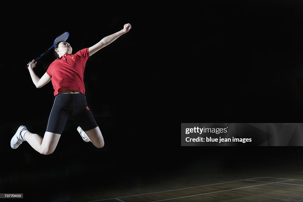 Young woman leaps high in the air and prepares to smash a shuttlecock during a game of badminton.