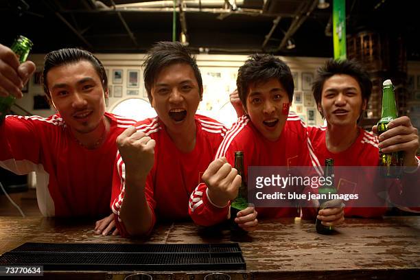 group of sports fans in matching uniforms pose for the camera at a sports bar - beer bottle mouth stock-fotos und bilder