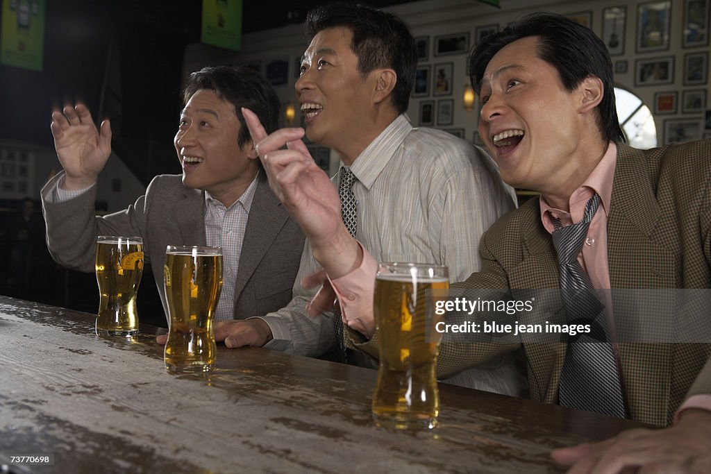 Three businessmen enjoy a game over beers at a sports bar