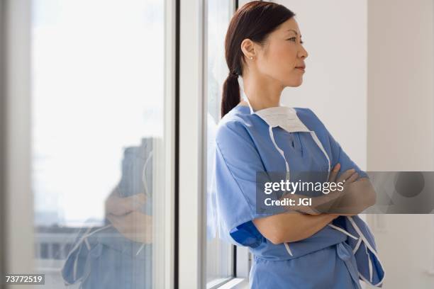 asian female doctor leaning against window with arms crossed - nurse thinking stock pictures, royalty-free photos & images