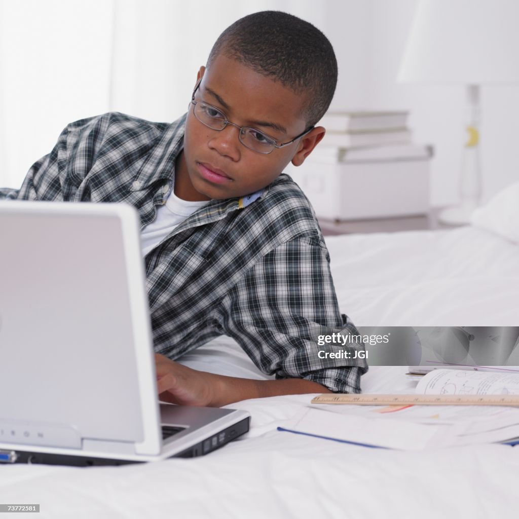 African boy studying with laptop on bed