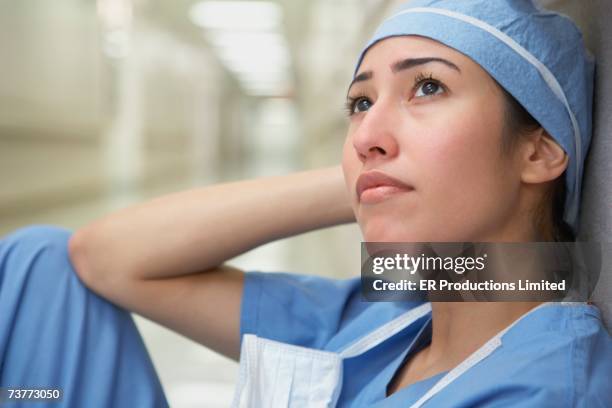 hispanic female doctor sitting against wall looking up - nurse thinking stock pictures, royalty-free photos & images