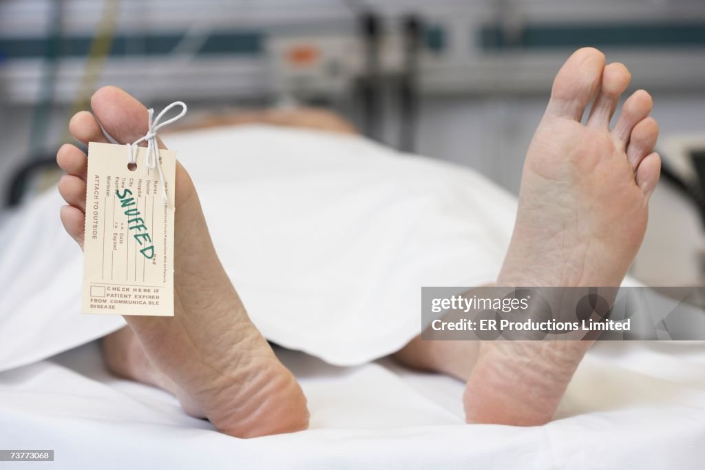 Close up of dead man's feet with toe tag reading Snuffed