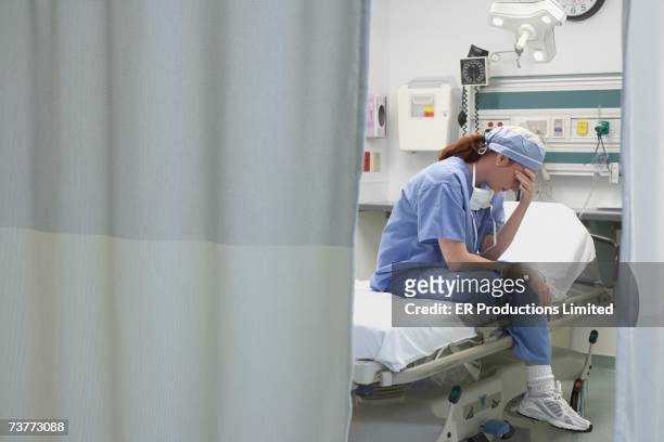 View through privacy curtains to female doctor sitting with head in hand