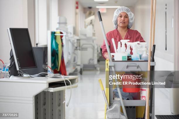 hispanic cleaning woman pushing cart in hospital corridor - criada fotografías e imágenes de stock