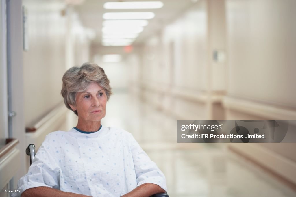 Senior female patient sitting in wheelchair at hospital corridor