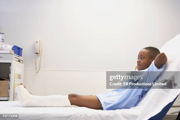 african boy with broken leg laying in hospital bed - boy sitting on bed stock-fotos und bilder