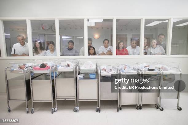 new parents watching babies in hospital nursery - service de maternité photos et images de collection