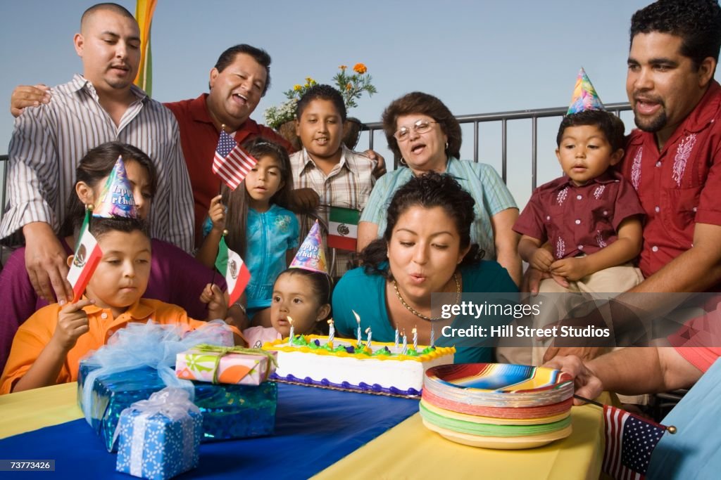 Young Hispanic woman blowing out candles on birthday cake with family