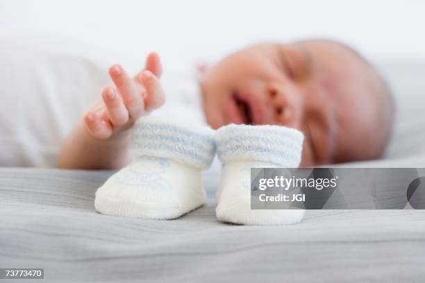 close up of baby booties next to sleeping newborn baby - baby booties stock pictures, royalty-free photos & images