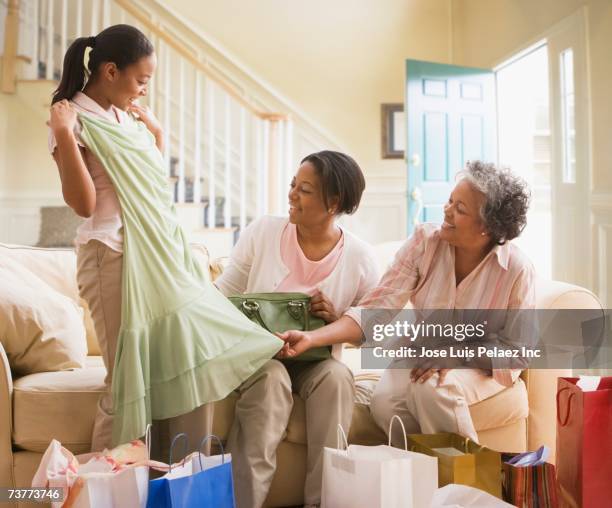 three generations of african women looking at new clothing - generationsunterschied stock-fotos und bilder