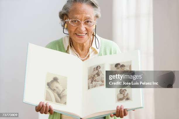 senior african woman holding photo album - waist up photos stock-fotos und bilder