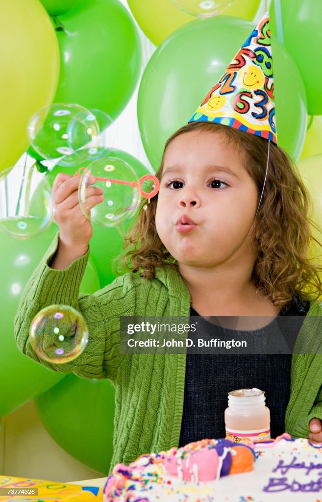 Young Hispanic girl blowing bubbles at birthday party
