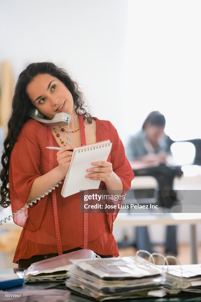 Hispanic seamstress using telephone in design workshop