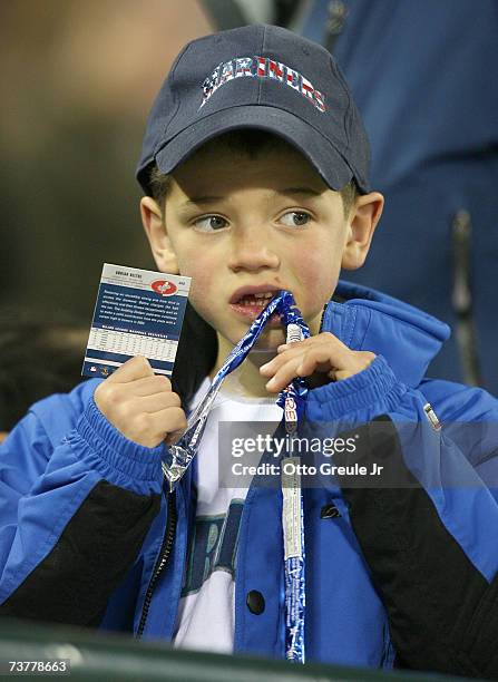 Young fan eats licorice while holding a baseball card during the seventh inning stretch on opening day during the game between the Seattle Mariners...