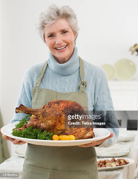 portrait of senior woman holding thanksgiving turkey - cooked turkey white plate stockfoto's en -beelden