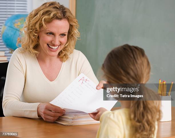 female teacher handing paper back to student - tetra images teacher stock pictures, royalty-free photos & images