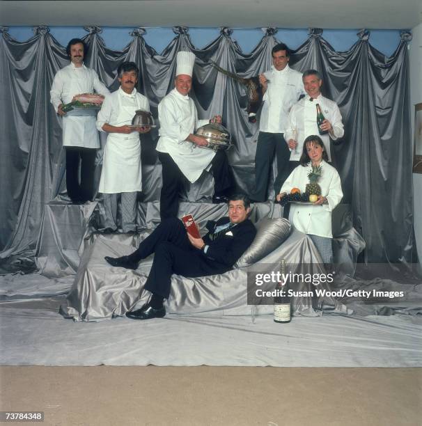 American lawyer and restaurant review compiler Tim Zagat reclines on a silver pillow as five men and a woman dressed in chef's whites stand around...